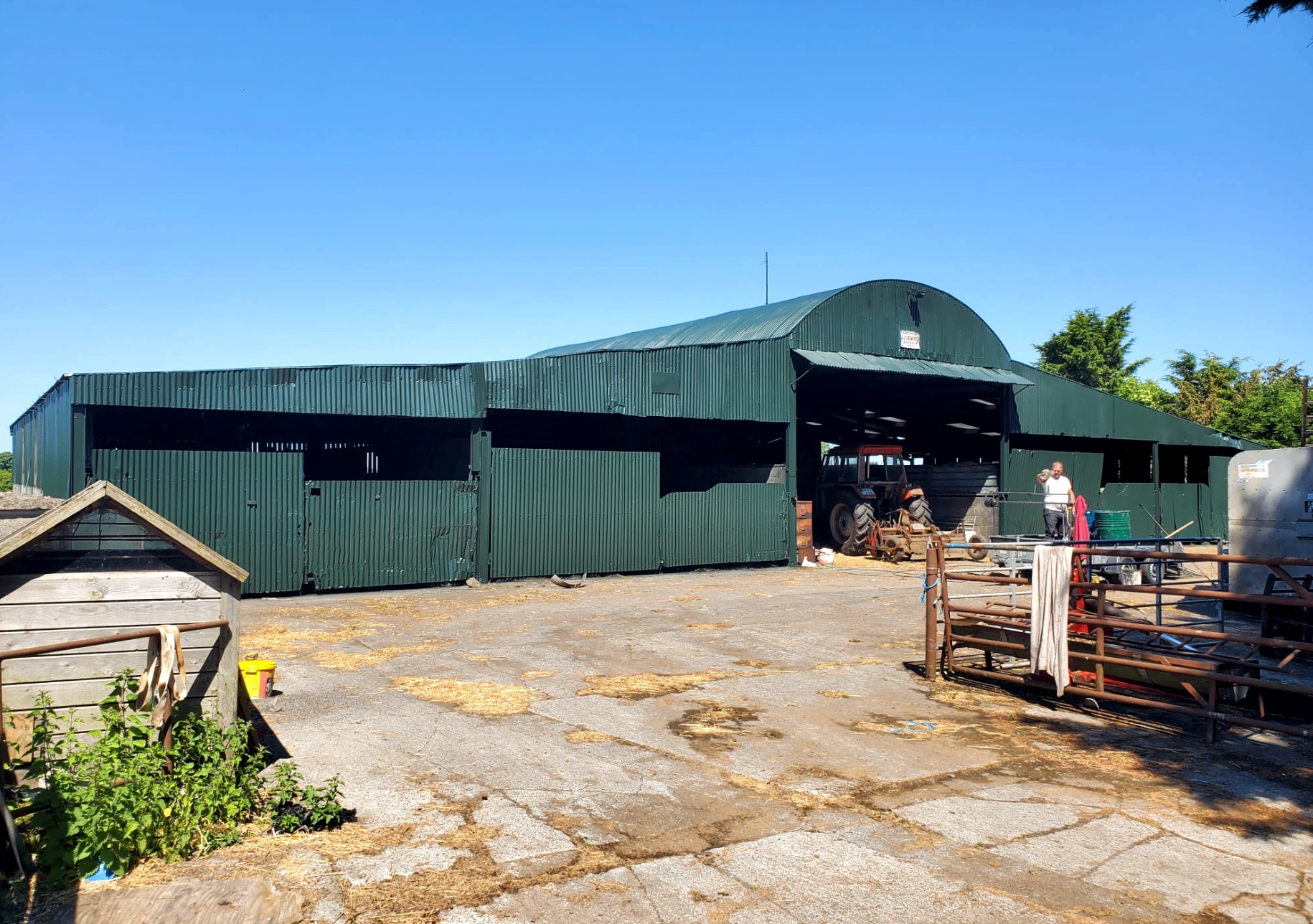 Large green farm shed with a tractor under a bright blue sky